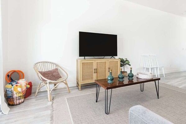 A living room with a flat-screen TV, wicker chair, wooden cabinet, and a coffee table. - The Heart of California w/ BBQ Grill & Hot Tub (Tulare)