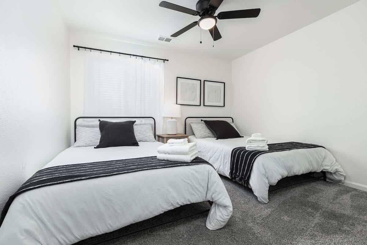 A hotel room with two beds, a ceiling fan, and a window with curtains.