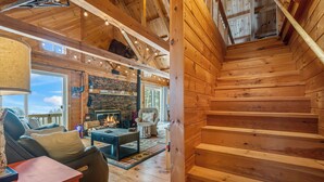 A wooden interior with a fireplace, seating area, and a staircase. - A Lookout at 'The Overlook' - Fall in love with this Rangeley cabin! (Rangeley)