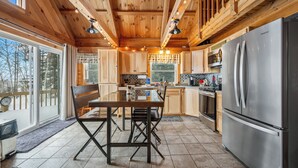 A wooden cabin interior with a dining table, chairs, a refrigerator, and a kitchen area. - A Lookout at 'The Overlook' - Fall in love with this Rangeley cabin! (Rangeley)
