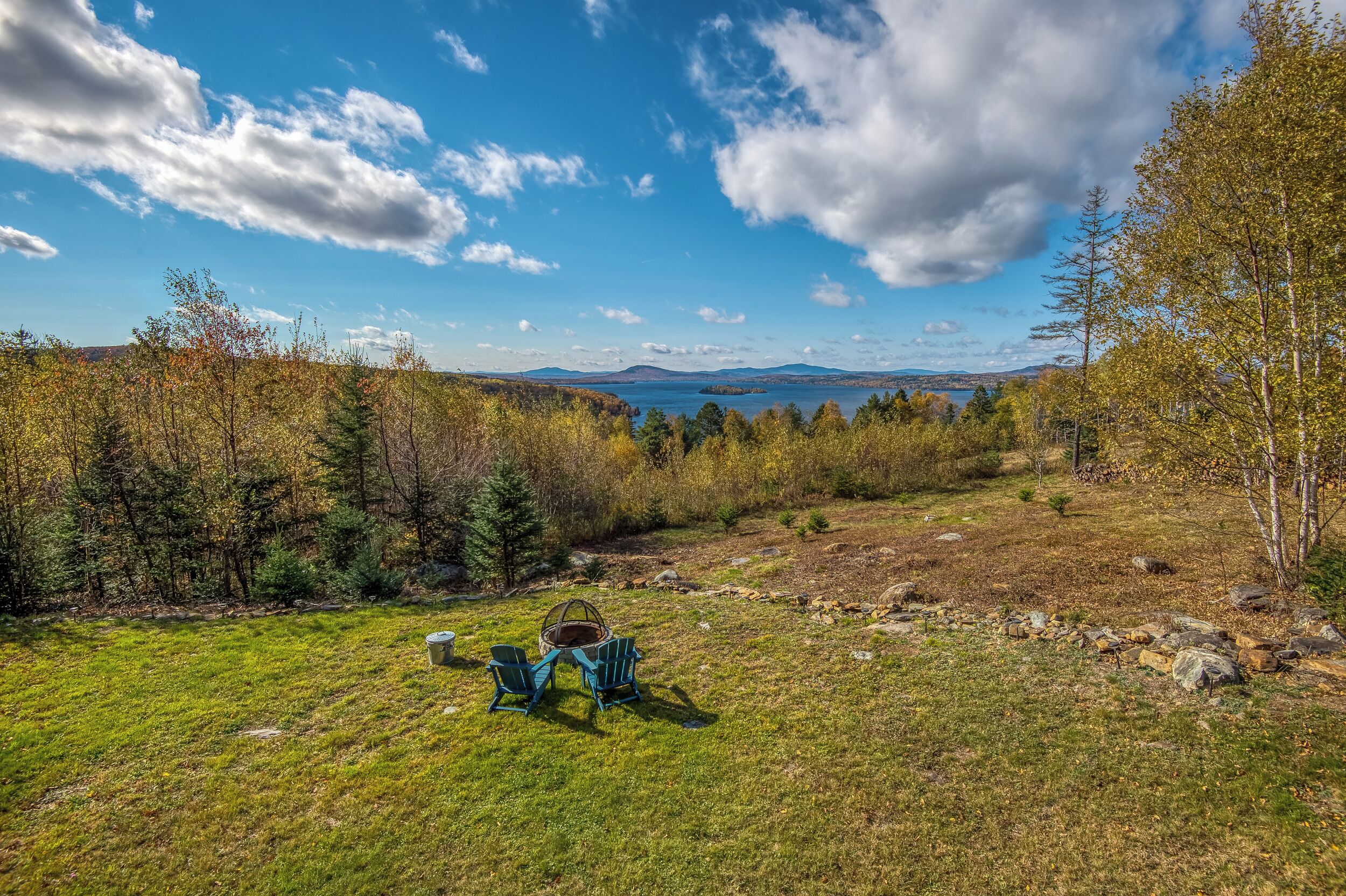 A campsite with two Adirondack chairs and a basket, surrounded by trees and a clear sky.