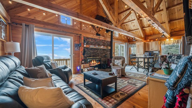A cozy cabin interior with a fireplace, leather sofa, wooden floors, and a dining area. - A Lookout at 'The Overlook' - Fall in love with this Rangeley cabin! (Rangeley)