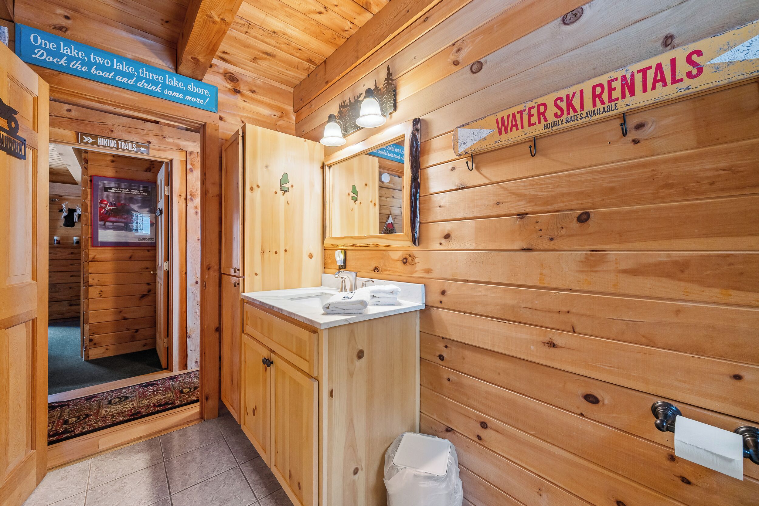 Interior de una cabaña de madera con un letrero de alquiler de esquíes acuáticos, un lavabo y un espejo.
