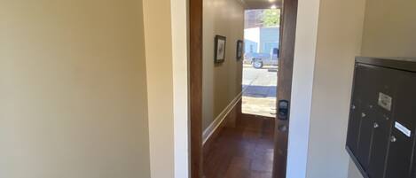A hallway with a wooden door, a mailbox, and a view of the outside.