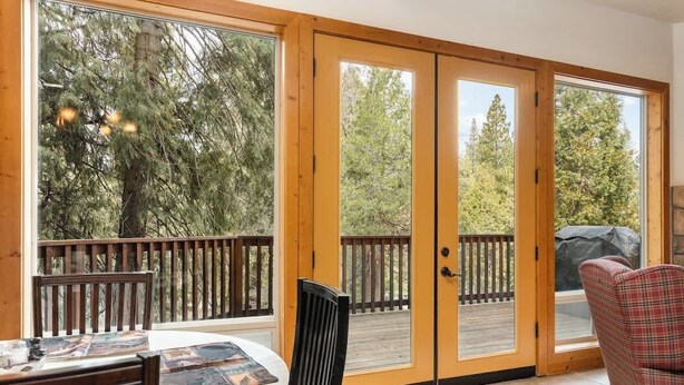A room with a wooden deck, a dining table with chairs, a sofa, and large sliding glass doors leading to an outdoor deck. - Mins to Lake, enjoy Shaver at PJ's Retreat! (Shaver Lake)
