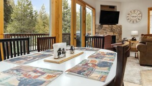 A dining area with a large table, chairs, and a view of trees through large windows. - Mins to Lake, enjoy Shaver at PJ's Retreat! (Shaver Lake)