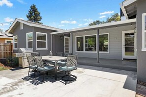 A patio with a table and chairs, a grill, and a covered area with windows.