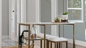 A modern dining area with a wooden table and bench, a small shelf with decorative items, and a view of the outdoors through large windows.