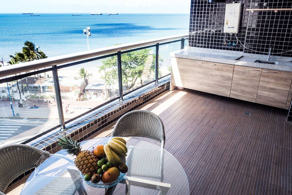 A balcony with a view of the sea, a table with fruit, and a modern kitchen area.