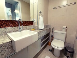 Et badeværelse med en hvid vask, toilet og bruseområde.