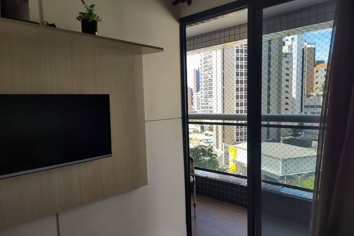 A balcony with a view of tall buildings, a TV mounted on the wall, and a potted plant on the ledge.