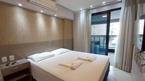 Ett hotellrum med en stor säng, en TV, en luftkonditioneringsanläggning, ett litet skrivbord med en stol och en balkong med utsikt.