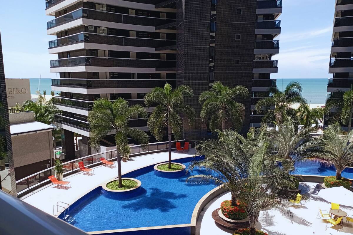 A modern hotel with a rooftop pool area featuring palm trees and sun loungers.