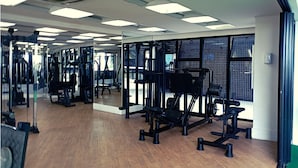 Ett gym med spegelbeklädda väggar, träningsutrustning och ett trägolv.