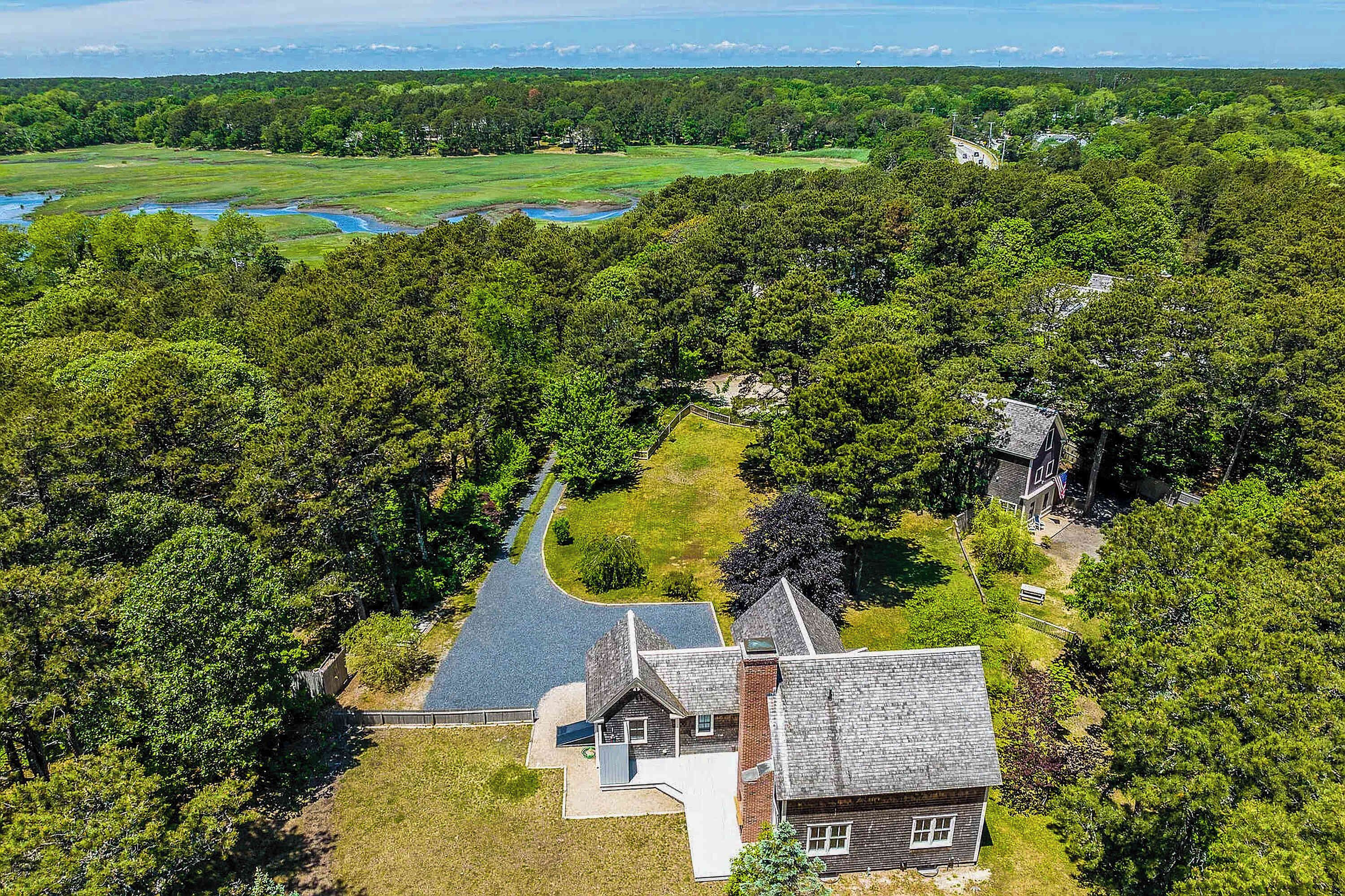 An aerial view of a property with a large house, a driveway, and surrounding wooded area.