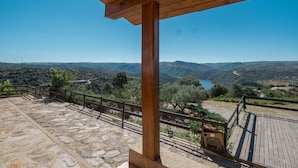 Una terraza empedrada con barandas de madera y vistas a un valle con montañas y un lago.