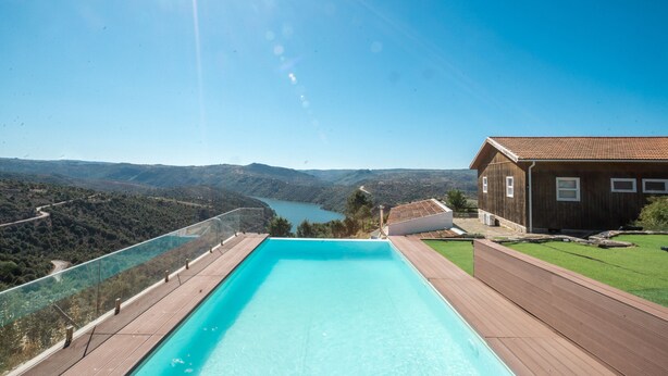 Una piscina con cubierta de madera, rodeada por una casa de madera con techo de tejas, con vistas a un valle y un lago.