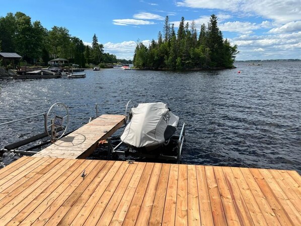 A wooden dock extending into a lake with a covered boat and a small boat docked nearby.
