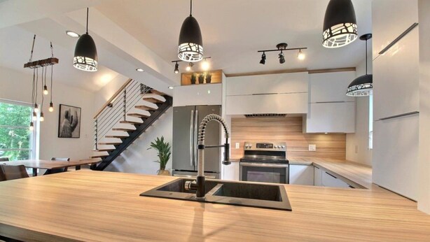 Una cocina moderna con una isla central, electrodomésticos de acero inoxidable y una escalera que sube a un nivel superior.