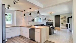 Una cocina moderna con una isla central, iluminación colgante y un comedor con sofá y mesa de centro.
