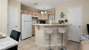 Een moderne keuken met een centraal eiland, barstoelen en een eethoek met een tafel en stoelen.