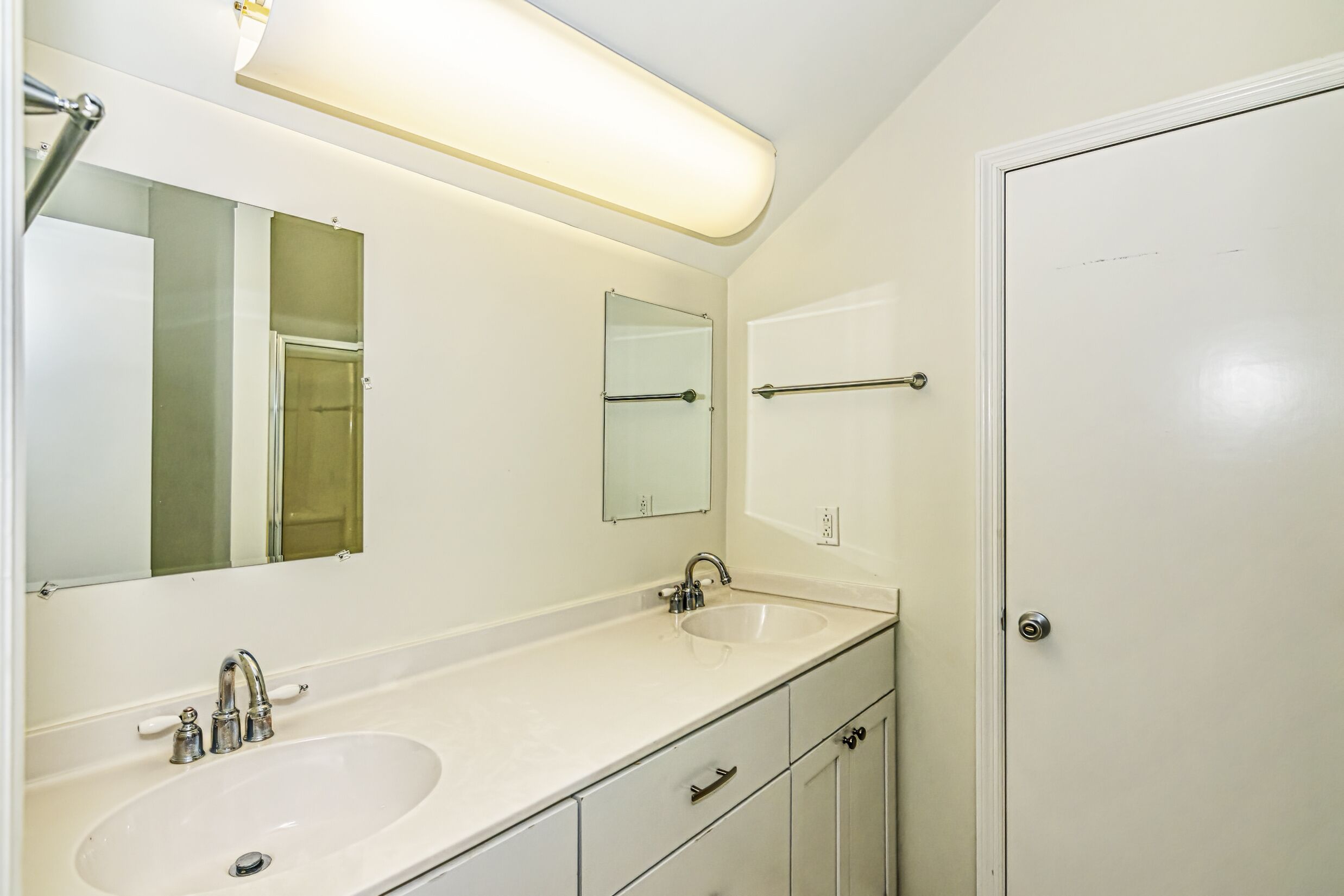 Une salle de bain avec deux lavabos, un miroir et une porte.