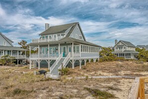 Una casa sulla spiaggia a due piani con un portico coperto e una scala che conduce al piano superiore.