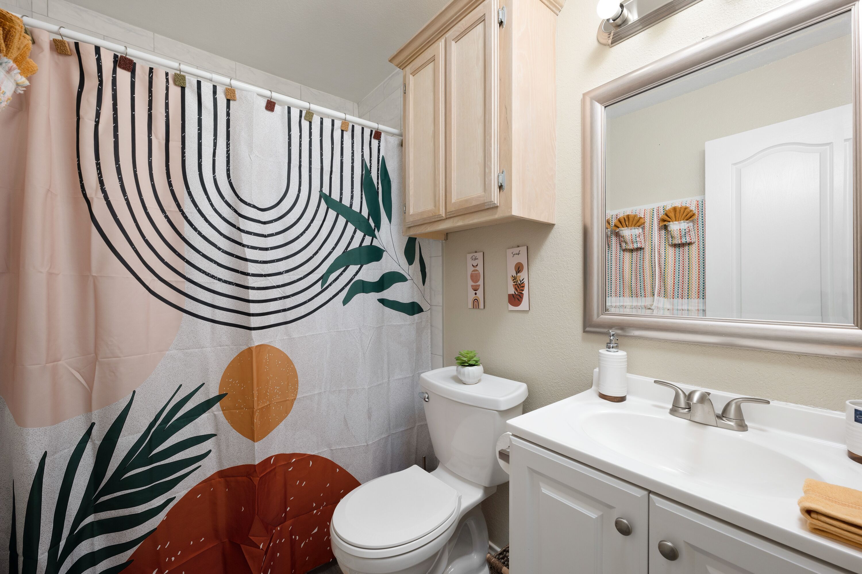 A bathroom with a toilet, sink, mirror, and a shower curtain with a leaf pattern.