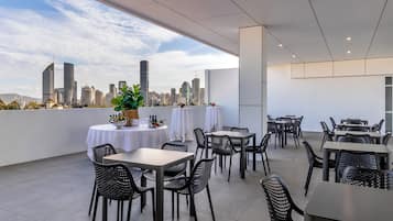 Ein Essbereich im Freien mit Tischen und Stühlen, Blick auf eine Stadtlandschaft und modernes Architekturdesign.
