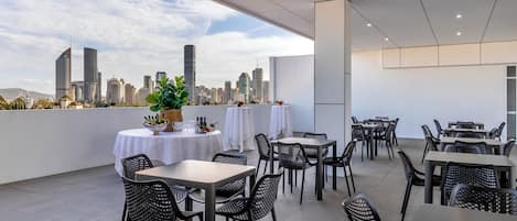 An outdoor dining area with tables and chairs, a city skyline view, and a modern architectural design.