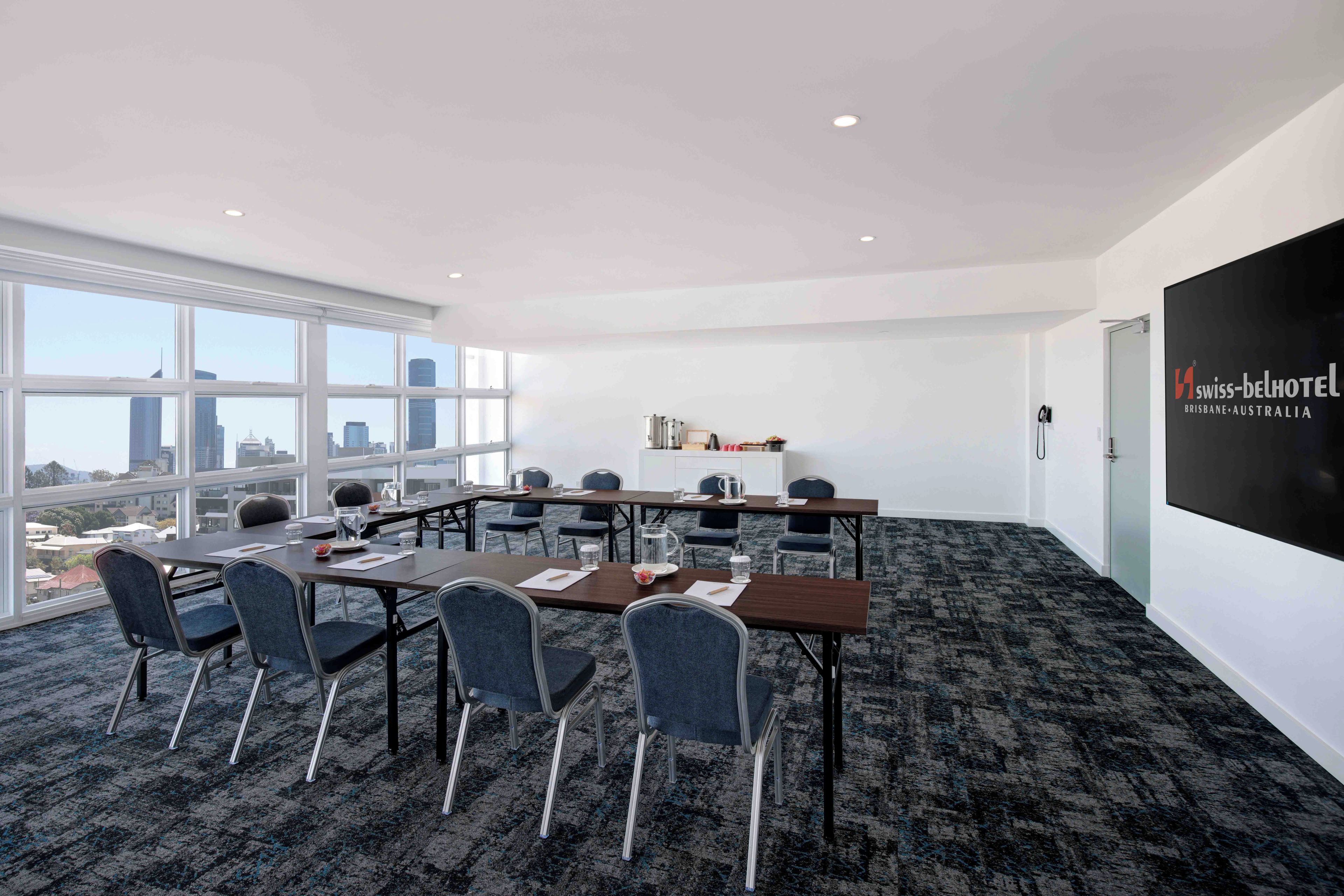 A conference room with a city view, equipped with tables, chairs, and a projector screen.