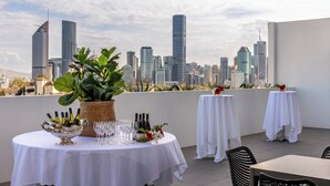 Une terrasse sur le toit, avec des tables dressées pour le dîner, une grande plante en pot et une vue panoramique sur la ville.