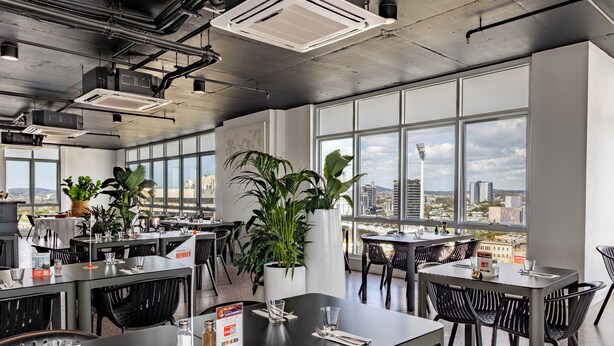 Un espace repas moderne avec de grandes fenêtres, des chaises noires et des plantes en pot.