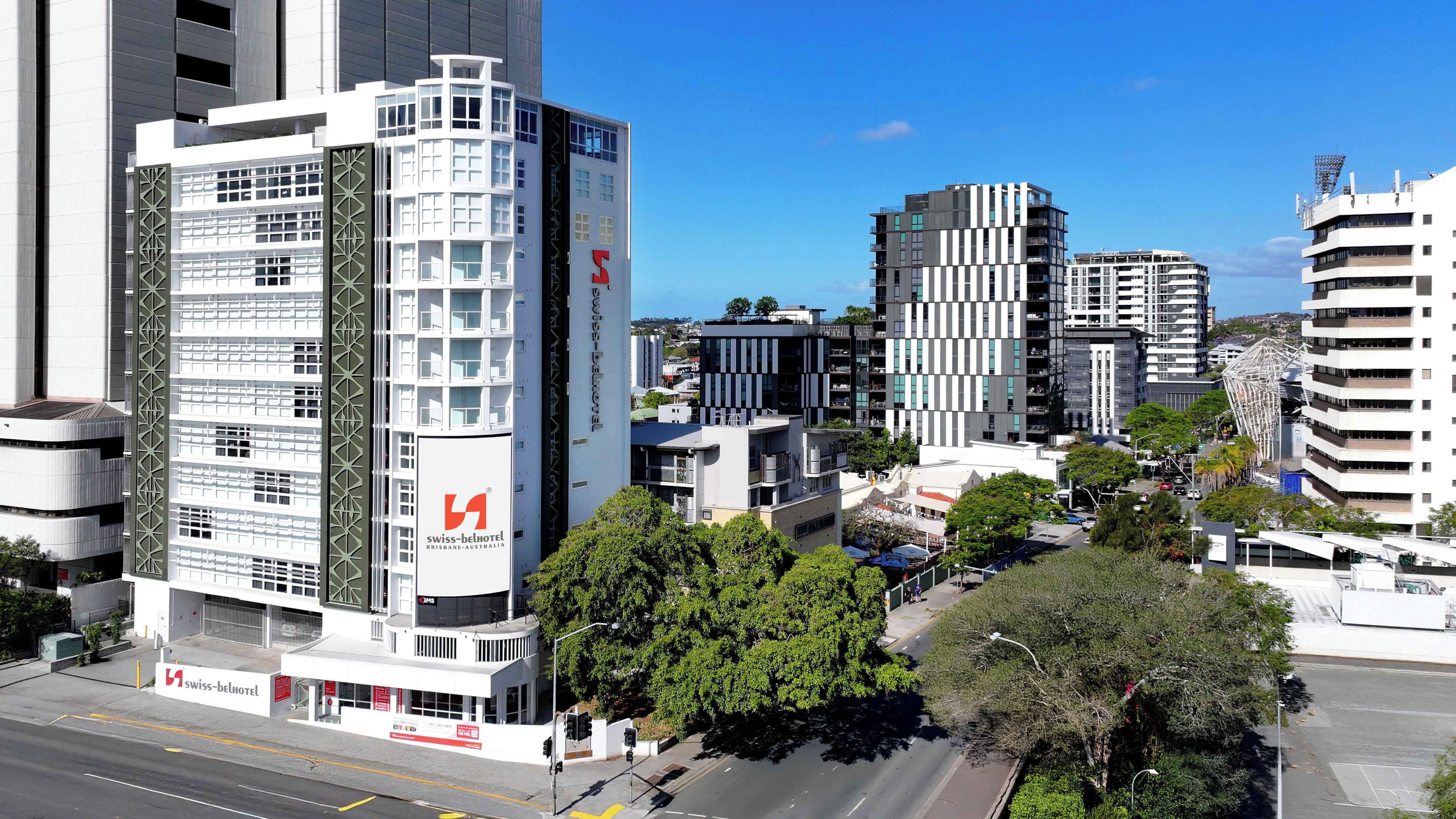 Un moderno edificio de hotel con varios pisos, un logotipo destacado y una vista despejada del entorno urbano.