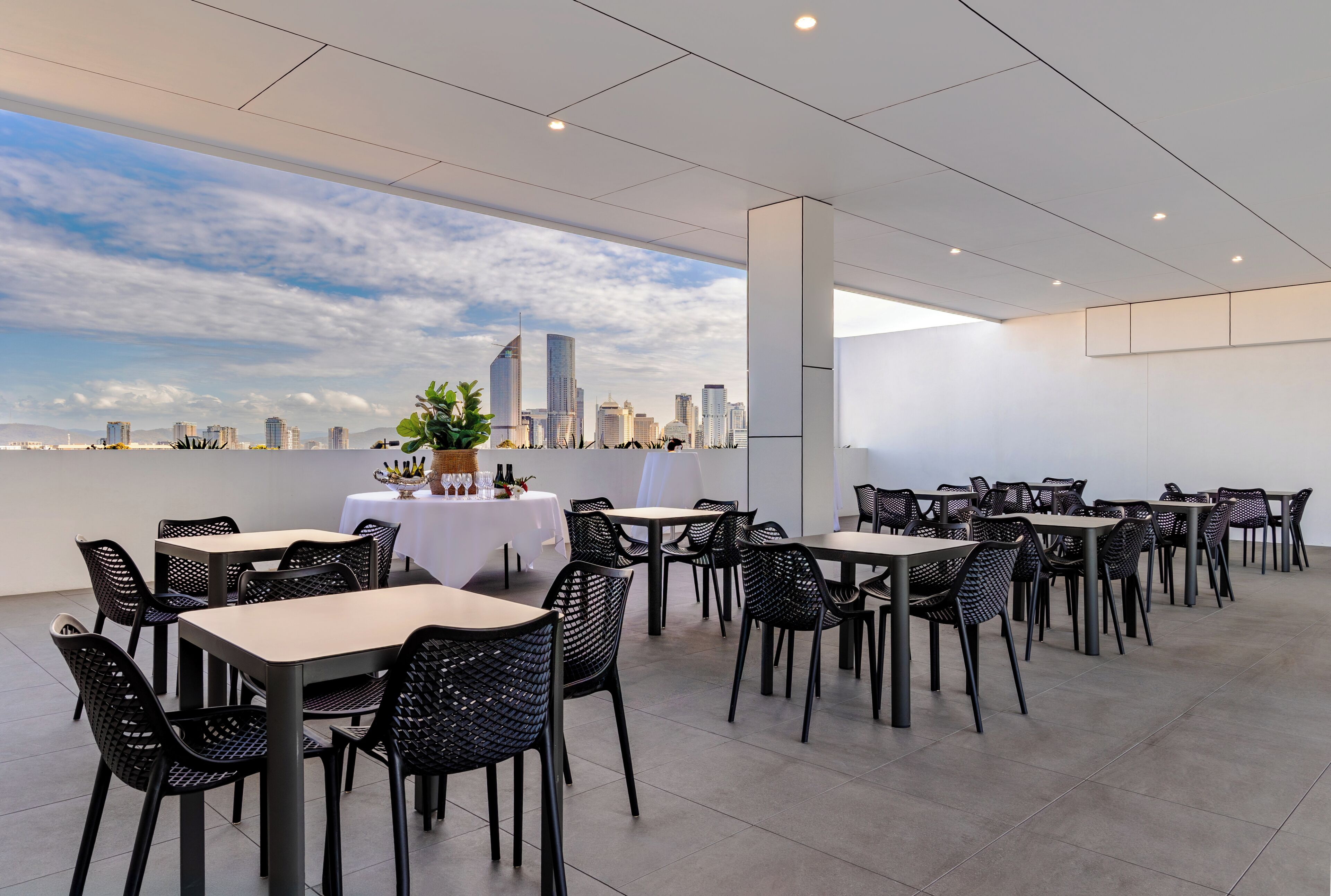 Un espace de restauration moderne, avec des tables et des chaises, une vue sur les toits de la ville et un plafond blanc.