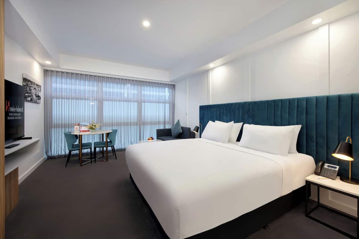 Une chambre d’hôtel moderne dotée d’un grand lit, d’un bureau avec une chaise, d’une télévision et d’une fenêtre avec des rideaux légers.