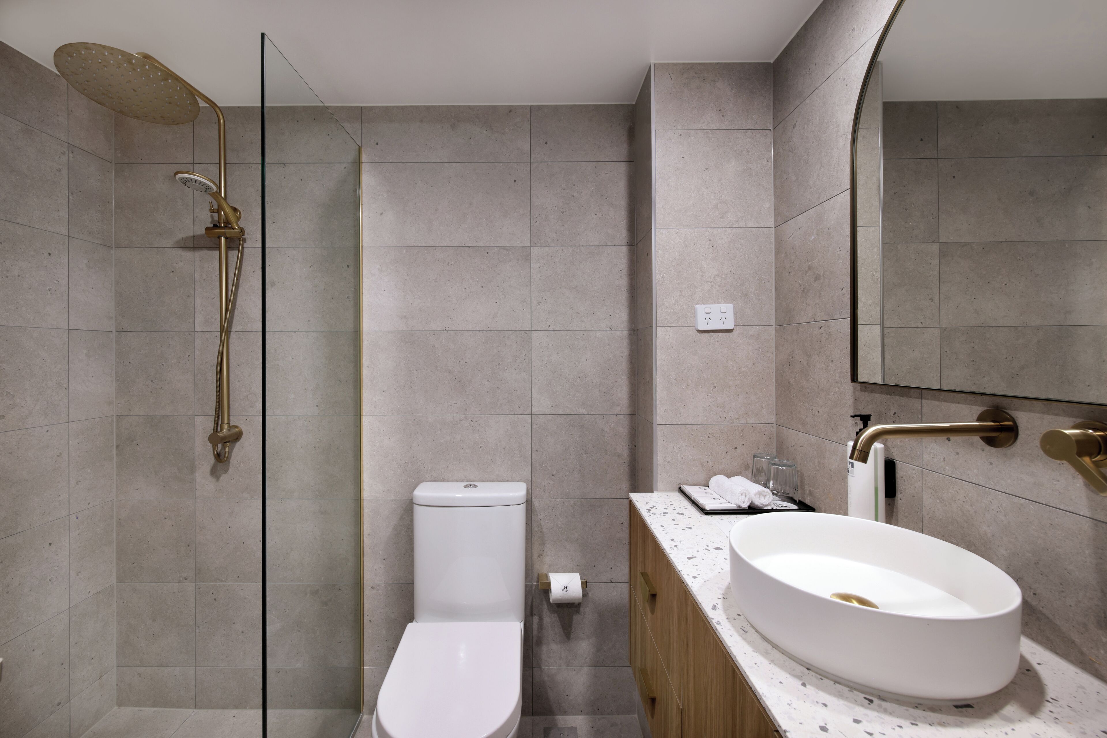 A modern bathroom with a freestanding toilet, a wall-mounted sink, and a shower with a gold showerhead.