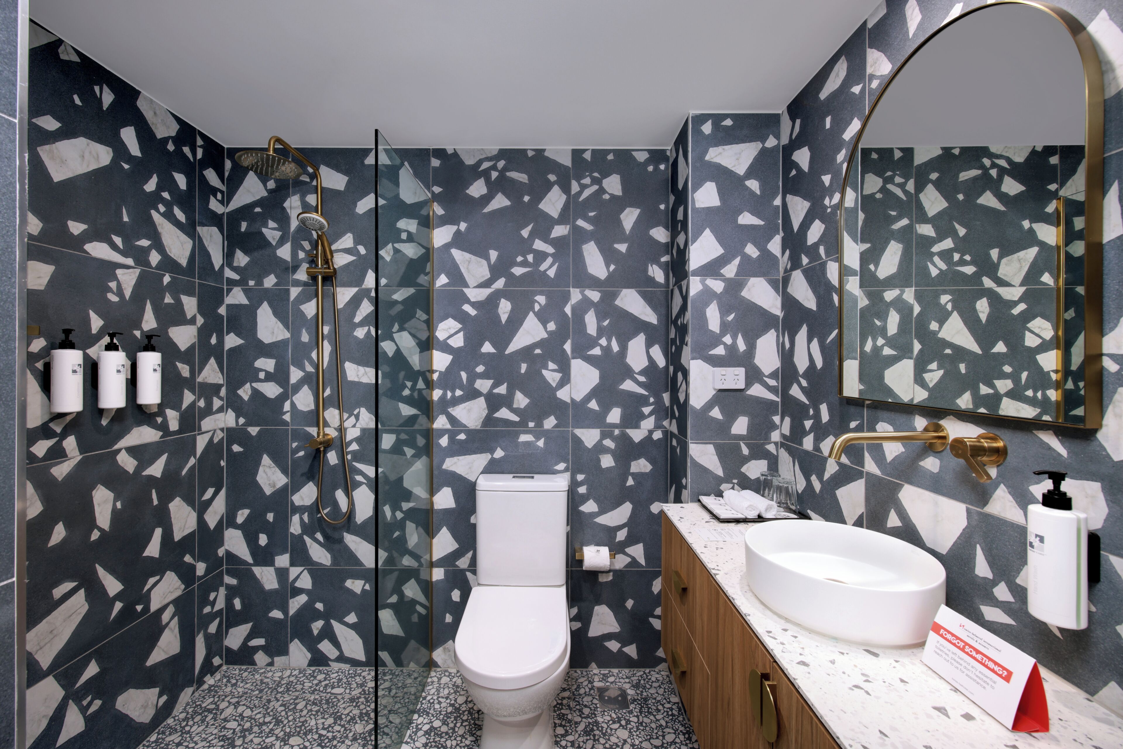 Ein modernes Badezimmer mit einer weißen Toilette, einer Dusche mit goldfarbenem Wasserhahn und einem Waschbecken mit Marmorplatte.