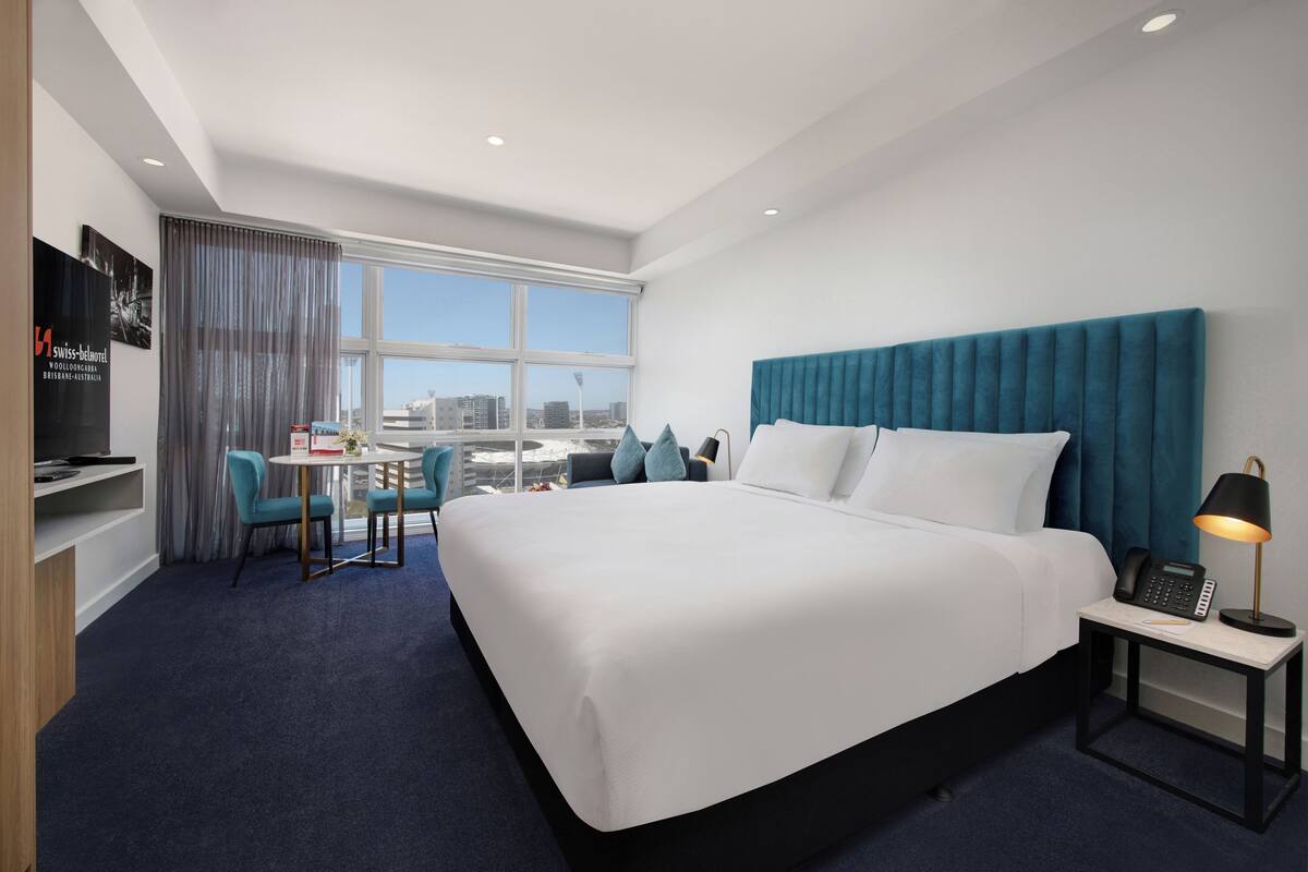 Une chambre d’hôtel avec un grand lit, un bureau avec une chaise, une télévision et une fenêtre donnant sur la ville.