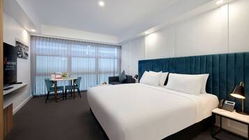 A hotel room with a large bed, a desk with a chair, a television, and a window with curtains.