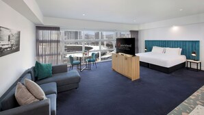 Une chambre d’hôtel moderne dotée d’un grand lit, d’une télévision, d’un canapé et d’un balcon offrant une vue sur la ville.