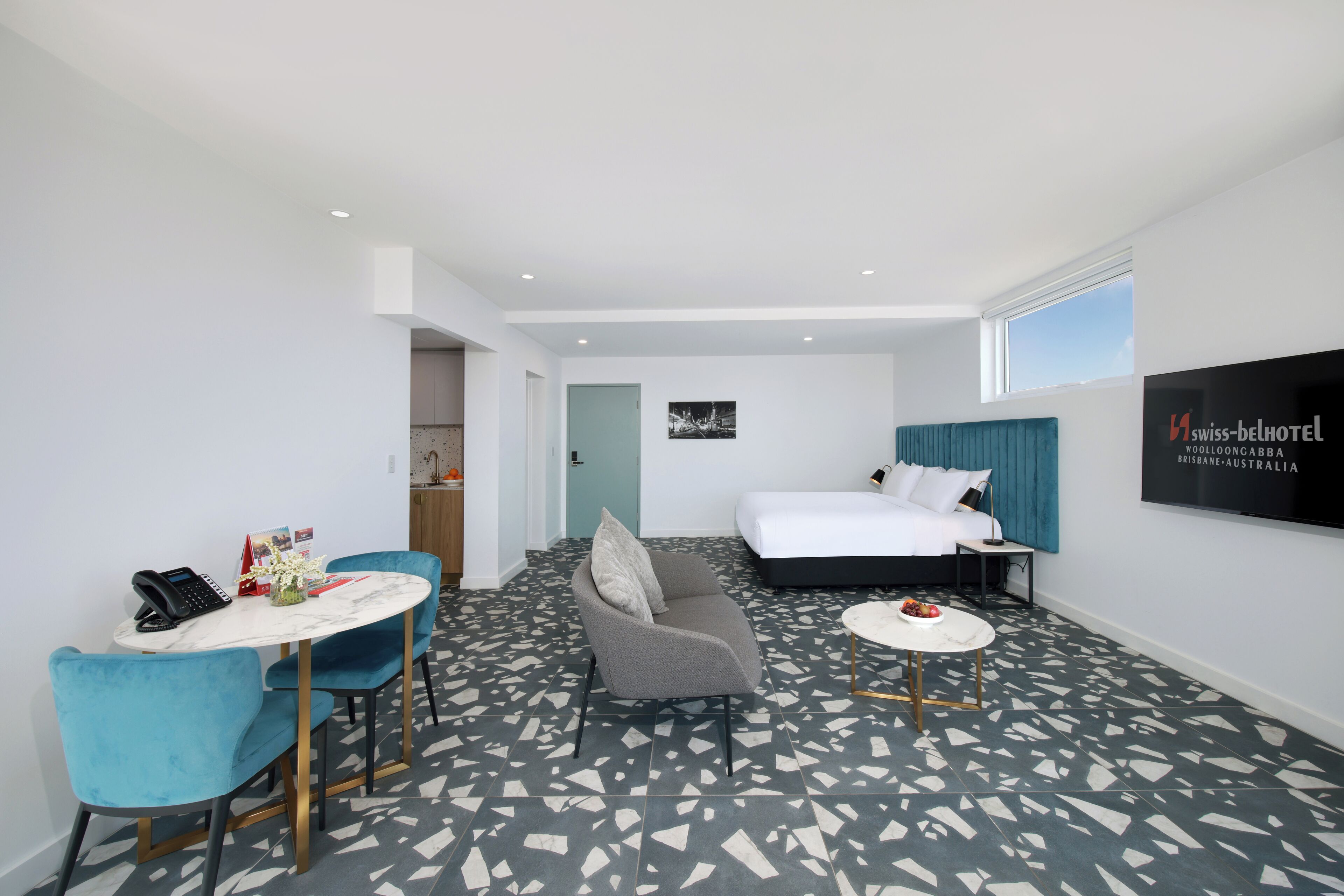 A hotel room with a bed, a sofa, a dining table, and a TV.