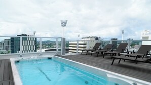 Une piscine sur le toit, avec une terrasse en bois, des chaises longues et une vue sur la ville.