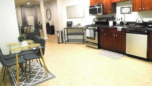A modern kitchen with wooden cabinets, a microwave, stove, and a dining area with a glass table and chairs.