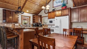 Een ruime keuken met houten kastjes, een centraal eiland en een eethoek met houten stoelen.