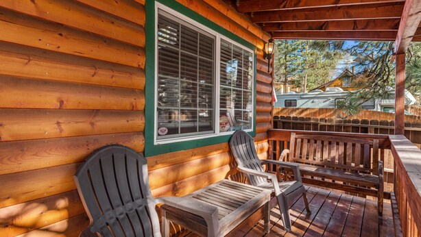 Een houten chalet met een veranda, voorzien van Adirondack stoelen en een houten tafel.