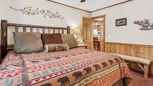 Een slaapkamer met een houten hoofdeinde, een bed met een bedekker met een patroon, een bankje, een lamp en een deur naar een andere kamer.