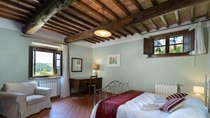 Een slaapkamer met een bed, een bureau, een stoel, een radiator en een raam met uitzicht op groen.