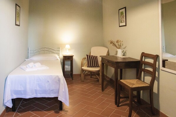 Una habitación con una cama, una silla, una mesita y un espejo.