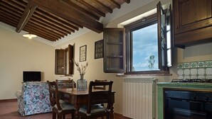 Un comedor con una mesa y sillas de madera, un jarrón con plantas secas y una ventana con vista a árboles.